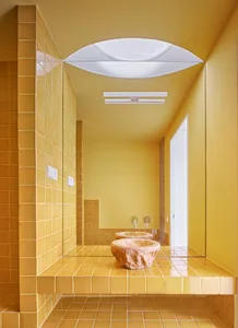 A minimalist bathroom with yellow ceramic tiles, a stone sink, and a large mirror.