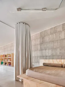 A minimalist bedroom with a fabric-covered bed on a concrete platform, featuring a concrete wall in the background and a ligh