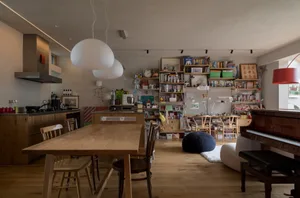 A modern living room with hardwood floors, a wooden table, chairs, and bookshelves filled with books.