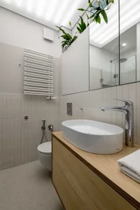 A modern minimalist bathroom with white ceramic tiles, a wooden vanity, and a sleek white sink.