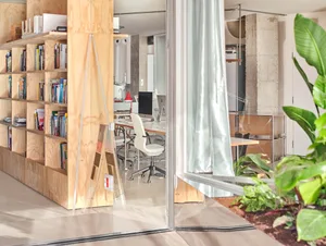 Interior view of a modern office space featuring concrete walls, glass partitions, wooden shelves, and a white chair.