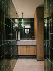 A modern bathroom with dark green ceramic tiles and a white concrete countertop with brass accents.