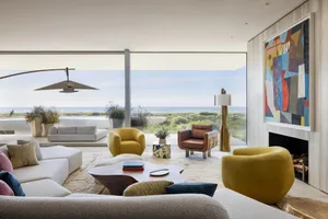A modern living room with a mix of materials, featuring a large window overlooking the ocean, comfortable furniture, and a vi