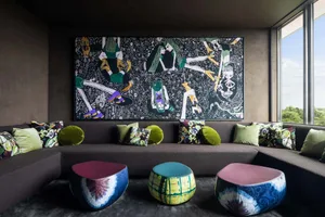 A modern lounge area featuring a large, colorful painting of figures, surrounded by a comfortable seating arrangement with pa