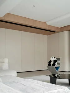 A modern minimalist bedroom with white cabinets, a white upholstered bed, and a white panda stuffed toy on a geometrically de