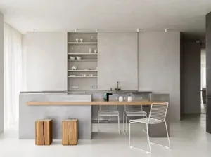A modern minimalist kitchen features a concrete island and white cabinets with a clean, uncluttered design.