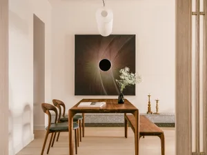 Modern minimalist dining room featuring a wooden table, chairs, and bench with a glass vase of flowers and a circular abstrac