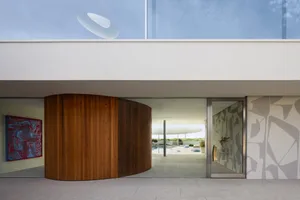 A modern residential exterior featuring large wooden columns and glass walls.