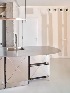 Minimalist kitchen featuring a metallic countertop and sink, with a concrete pillar and white walls.