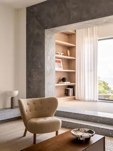 A minimalist living room with a terrazzo floor, curtains, and a bookshelf.