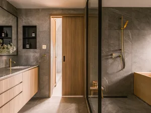 Modern bathroom interior with marble flooring, wooden accents, and gold fixtures.