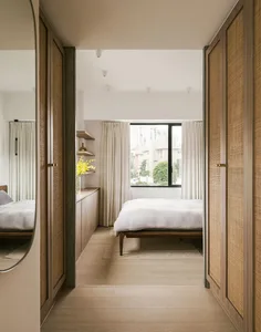 A modern residential bedroom featuring a bed with wood frame and cane-textile headboard, white bedding, and tall wooden wardr
