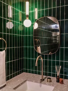 A modern bathroom with green tiles, a terrazzo countertop, and a round mirror.