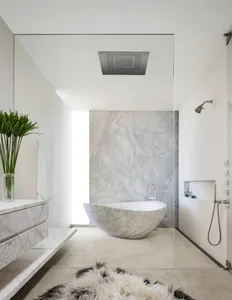 Modern minimalist bathroom with a freestanding marble tub, white walls, and a white marble pedestal sink.