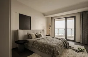 A minimalist bedroom featuring a textured fabric bed, abstract lighting fixture, and balcony view.