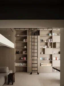 Minimalist living room with wooden bookshelves and ladder, featuring a grey couch and dark wooden stools.
