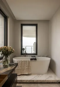 A modern bathroom interior featuring a freestanding marble tub and a vase of flowers on a marble counter.