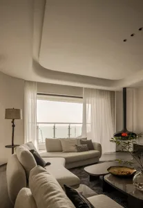 A modern living room featuring a white fabric sofa, glass coffee table, and large windows with a view of the ocean.