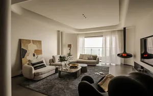 Modern living room with white sofas, decorative cushions, and a hanging fireplace.