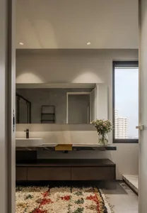 A modern minimalist bathroom featuring marble countertops, wooden cabinets, and a glass vase with flowers.