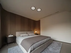 極簡臥室內，床上鋪著人字紋毯，搭配木質地板與單一燈具的小型床頭櫃