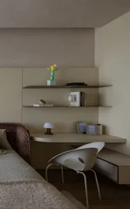 A minimalist bedroom with a built-in work space featuring neutral-toned shelves, a chair, and a bed with a quilted headboard.