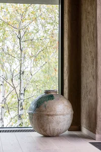 A round ceramic vase with green splatter sits in front of a window with a natural tree view.
