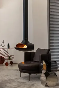 A modern living room featuring a black leather armchair, a metal coffee table, and a concrete floor, with a hanging fireplace