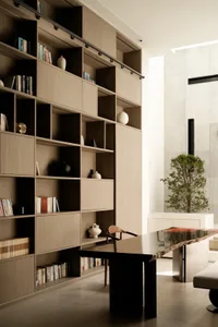 A modern library with wooden shelves and a black desk with a tree and bench.