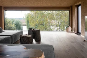 A modern living room with a wooden floor, large windows, and a view of nature.