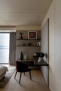 A modern minimalist bedroom featuring a wooden desk, chair, and shelves with decorative items.