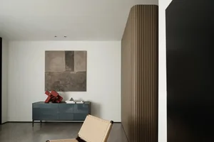 A minimalist bedroom with a modern design, featuring a wooden chair, a blue dresser, and a painting on the wall.