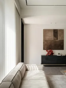 Minimalist living room with modern, neutral-colored sofa, concrete accent wall, and abstract artwork.