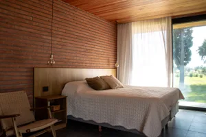 A minimalist bedroom featuring brick accent wall and wooden flooring, with a bed adorned by a white quilt and brown pillows.