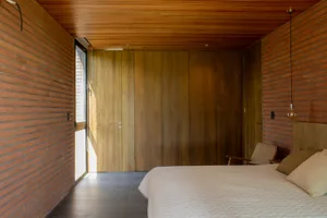 A minimalist bedroom featuring wood paneling, a large bed, and a small chair against a wall.