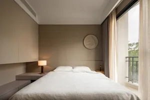 A modern bedroom with a neutral-colored wall, featuring a white bed and a simple decorative plate.