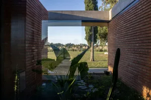 Modern exterior featuring brick walls, concrete walkway, glass doors leading to a residential lawn with greenery and trees.