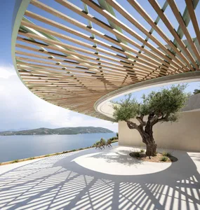 A modern lounge area with wooden slats and a single tree, overlooking a scenic body of water and distant mountains.