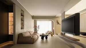 A modern living room with neutral tones, featuring a beige sofa, a black coffee table, and a large flat-screen TV.