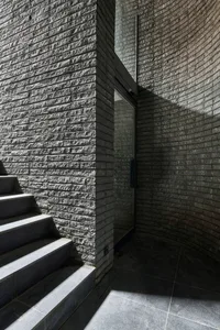 Modern entryway featuring dark gray stairs adjacent to a curved brick wall with a glass door.