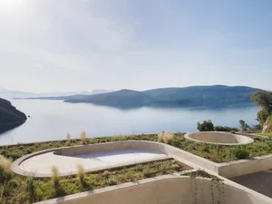 Concrete planters with green plants near a poolside area with a view of the ocean and mountains.