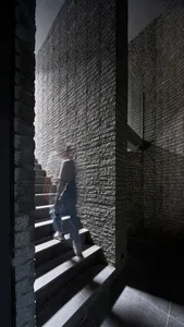 A person walking up a staircase in an urban industrial interior with brick and concrete walls.