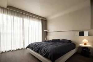Minimalist bedroom featuring a textured concrete bed platform, dark bedding, and a floor-to-ceiling window with sheer curtain