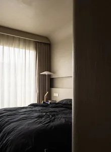 A minimalist bedroom with a textured wall, a bed with black bedding, and a lamp on a headboard.