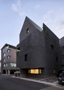 Modern architectural design featuring a black brick exterior with geometric windows and a sloped roof.