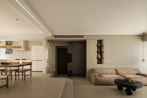 A modern minimalist living room featuring a beige sofa, black coffee table, and floating shelves.