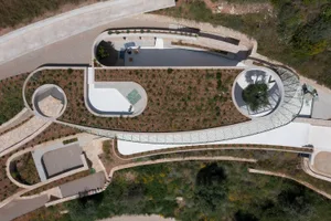 A modern park landscape with concrete pathways, stone walls, and lush green plants.