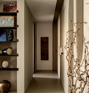 A modern, minimalist corridor with neutral-toned walls and floors, decorated with a few art pieces and a wooden wall panel.