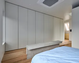 A minimalist bedroom features a concrete bed frame and sleek, white wardrobes.