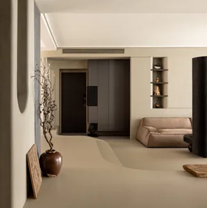 A minimalist living room with concrete walls and floor, featuring a beige couch, wooden accents, and sculptures.